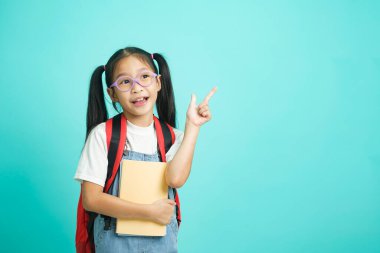 Smiling little girl in glasses pointing finger upward going to school, school concept. standing on a blue background.