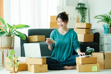 Young asian business owner working with calculator, The seller prepares the delivery box for the customer with postal parcel. Selling online and delivery.