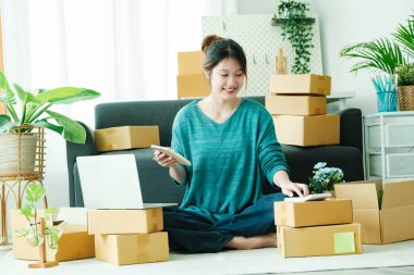 Young asian business owner working with calculator, The seller prepares the delivery box for the customer with postal parcel. Selling online and delivery.