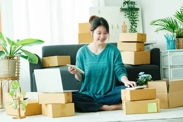 Young asian business owner working with calculator, The seller prepares the delivery box for the customer with postal parcel. Selling online and delivery.