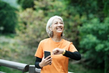 Happy athletic Senior woman checking her smartwatch in the park, Concept of a healthy lifestyle on retirement. health concept.