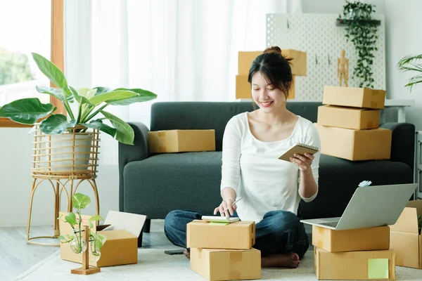 Young asian business owner working with calculator, The seller prepares the delivery box for the customer with postal parcel. Selling online and delivery.