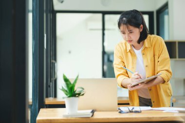 Gülümseyen Asyalı iş kadını ev bilgisayarında çalışıyor. Genç Asyalı öğrenci ya da uzaktan öğretmen bilgisayar kullanıyor. İnternette öğrenim görüyor, sanal eğitim veriyor, internet üzerinden eğitim alıyor..