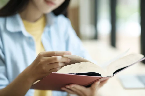 Close up of woman studying and reading book beside the windows. Woman holding and reading book for school study while sitting beside windows. learning concept.