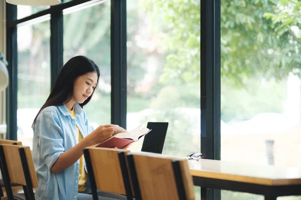Молода Азіатка Читає Книгу Сидить Перед Ноутбуком Столі Біля Вікон — стокове фото