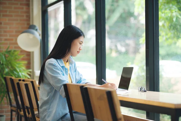 Щаслива Молода Азіатка Сидить Столом Пише Блокноті Перед Ноутбуком Студентське — стокове фото
