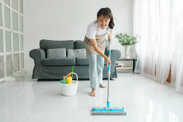 Young woman in casual clothes cleaning wasing floor using mop with cleaning solution in living room at home. Woman doing housechores at home. Housekeeping concept.