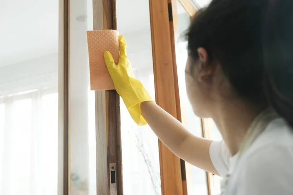 窓スプレーを使用して自宅で若い女性が窓を掃除し 黄色の手袋を着用 女性はそれにきれいな溶液を噴霧し 黄色のラグで拭くことにより 窓ガラスの掃除の家事を行うことを楽しむ — ストック写真