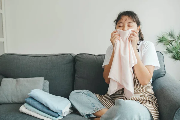 Young woman on sofa smell clean laundry at home in living room after doing housechores. Lady happy and satisfied when smell clean laundry.