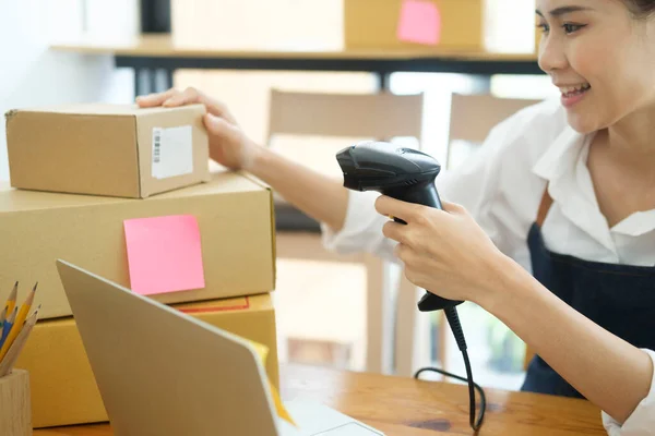 Female small online business owner holding scanner scanning parcel barcode tag before shipment at workplace. Woman selling products online, scanning parcel barcode. Online business concept.