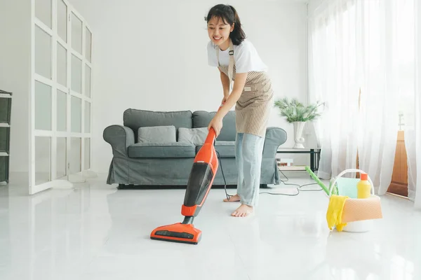 Young woman in casual clothes cleaning floor using vacuum cleaner and cleaning equipments in living room at home. Housekeeping concept.