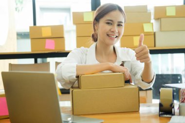 İnternette ürün satan ve el hareketi yapan Asyalı kadın bir işadamı. İnternetteki işinde iyi iş çıkaran ve baş parmağını gösteren bir kadın. Çevrimiçi iş kavramı.