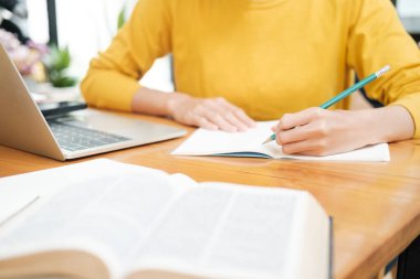 İnternette okuyan genç bayanı kapat ve masada otururken dizüstü bilgisayar ve ders kitapları kullanarak kitap üzerine notlar yaz. Çevrimiçi öğrenme kavramı.