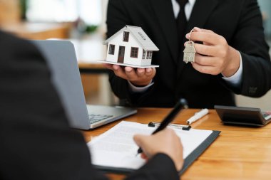 Emlakçı, ev modelini ve ev anahtarlarını ev almak için ev kredisi sözleşmesini tartıştıktan ve imzaladıktan sonra müşteriye vermek üzere tutuyor. Emlak kavramı.