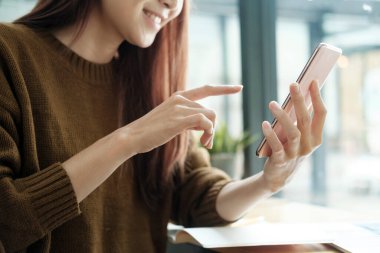 Genç Asyalı kız öğrenci dizüstü bilgisayar kullanıyor ve cep telefonu tutuyor. İş ve eğitimi hakkında bilgi edinmek için internette sörf yapıyor. Çevrimiçi öğrenme kavramı.