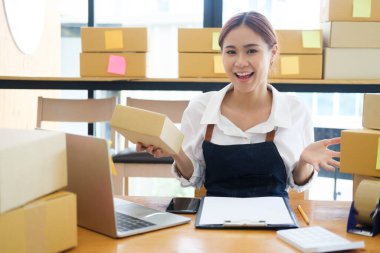 Asyalı kadın online iş sahibi kameraya mutluluk ve neşeyle bakıyor ve teslimat kutularını gösteriyor. Çevrimiçi iş kavramı.