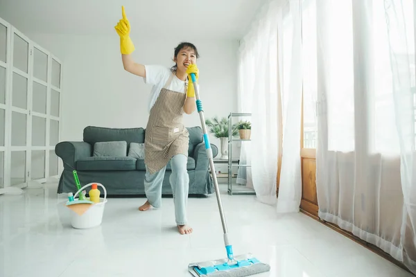 自宅でモップを使って掃除しながら楽しい歌を歌う陽気な若い女性 カジュアルな服やエプロン洗浄で女性 ダンス そしてクリーニング中に楽しみを持っています 家事の概念 — ストック写真