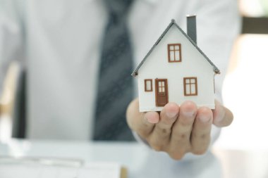 Emlakçı ev modelini ve anahtarlarını tutuyor, danışmanlık yapıyor ve müşteriyle ev almak için sigorta sözleşmesi imzalama kararını tartışıyor. Emlak kavramı.