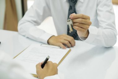 Emlakçı, ev almak için ev kredisi sözleşmesi imzaladıktan sonra müşteriye vermek üzere evin anahtarlarını tutuyor. Emlak kavramı.
