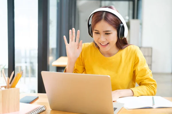 若いアジアの女性学生は 職場の机に座っている間にヘッドフォンを装着したラップトップを使用してビデオ通話を持って オンラインで勉強し 学習します オンライン学習の概念 — ストック写真