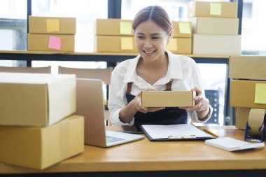 Asyalı kadın çevrimiçi iş sahibi video üzerinden ürün satıyor, konuşuyor ve müşteriyle paket gösteriyor. Müşteri ile görüntülü konuşma yapan bir kadın dizüstü bilgisayarla ürün satışı yapıyor..