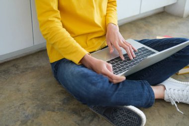 İnternette çalışan ya da okuyan genç bir kadın kendi yerinde dizüstü bilgisayarla araştırma ya da ödev yaparken yerde oturuyor. Çevrimiçi iş ve yaslanma kavramı.