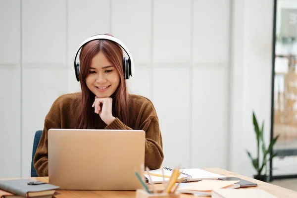 ヘッドフォンを装着したラップトップを使ってオンラインで勉強や仕事をしている若いアジアの女性は 職場だけで横になった教科書や文房具を机に座っています オンライン学習またはワークコンセプト — ストック写真