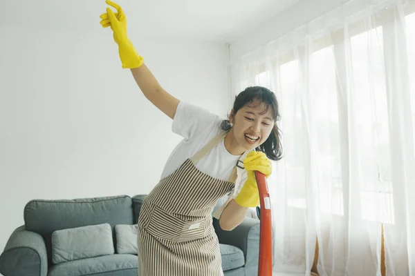 掃除機を使って自宅で掃除をしながら楽しく歌を歌う陽気な若い女性 カジュアルな服やエプロン洗浄で女性 ダンス そしてクリーニング中に楽しみを持っています 家事の概念 — ストック写真