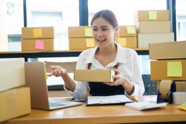 Asyalı kadın çevrimiçi iş sahibi video üzerinden ürün satıyor, konuşuyor ve müşteriyle paket gösteriyor. Müşteri ile görüntülü konuşma yapan bir kadın dizüstü bilgisayarla ürün satışı yapıyor..