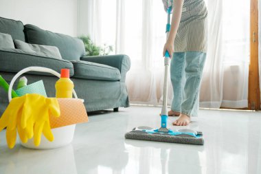 Günlük kıyafetlerle yerleri temizleyen, paspas kullanan, evdeki oturma odasında temizlik malzemesi kullanan genç bir kadın. Evde ev işleri yapan bir kadın. Oda servisi kavramı.