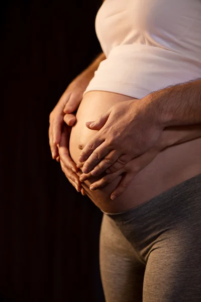 Mannelijke en vrouwelijke handen op zwangere buik. — Stockfoto