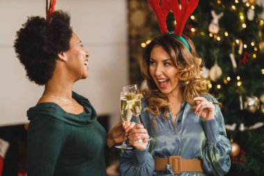 Çok ırklı bayan arkadaşlar Noel 'i ya da yeni yılı kutlamak için evde toplandılar. Şampanya ile kadeh kaldırıyorum..