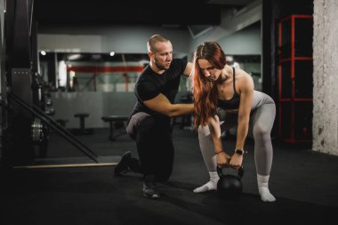 Spor salonunda kişisel antrenörle çalışan kaslı genç bir kadının fotoğrafı. Kettlebell ile egzersiz yapıyor..