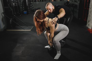 Spor salonunda ağırlık antrenmanı yapan genç kaslı bir kadını izleyip ona yardım eden spor eğitmeni..