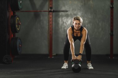 Bayan sporcu spor salonunda kettlebell ile çalışıyor..