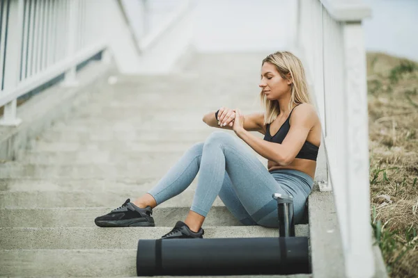 美丽健康的女人在经过艰苦的训练后 正在城市的桥上楼梯上休息 看着自己聪明的身体 — 图库照片