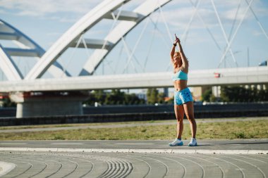 Yetişkin kadın nehir kenarındaki spor antrenmanı için ısınırken esneme egzersizleri yapıyor..
