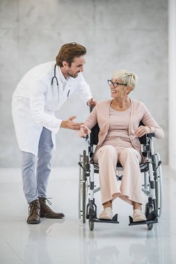 Tekerlekli sandalyedeki yaşlı bir kadına yardım eden genç bir doktor..