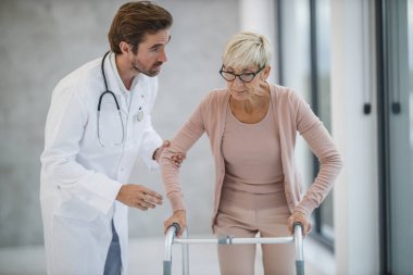 Genç bir doktorun, yaşlı bir kadın hastaya yürümesi için yardım etmesi..