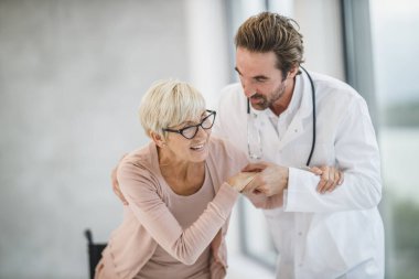 Tekerlekli sandalyedeki yaşlı bir kadına yardım eden genç bir doktor..