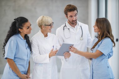 Farklı doktor ve hemşirelerden oluşan bir ekibin portresi bir arada duruyor ve hastanede dijital tablet kullanıyorlar..