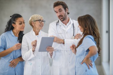 Farklı doktor ve hemşirelerden oluşan bir ekibin portresi bir arada duruyor ve hastanede dijital tablet kullanıyorlar..