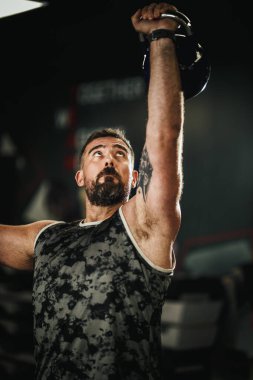  Spor kıyafetli kaslı adam spor salonunda ketlbell ile basın egzersizi yapıyor..