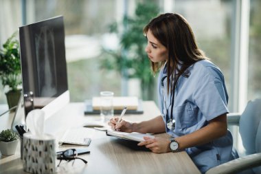 Çekici bir bayan hemşire hastanede masasında tek başına oturuyor ve bilgisayardaki röntgen görüntülerine bakıyor..