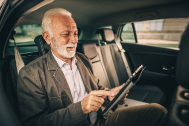 Başarılı bir kıdemli işadamının dijital tablet kullanırken sabah işe gidip gelirken arabanın arka koltuğunda oturması..