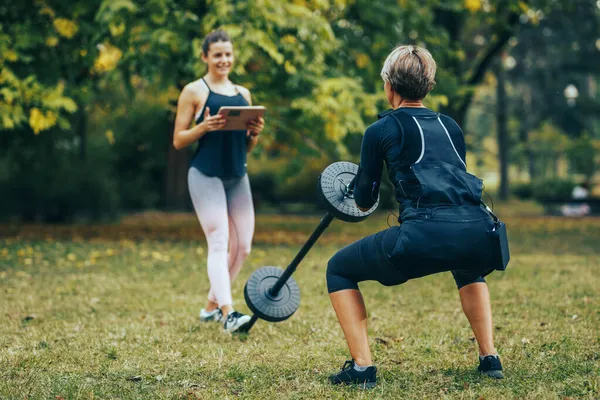 여자가 공원에서 조련사와 웅크리고 운동을 있는데 근육을 자극하기 Ems 시뮬레이터를 — 스톡 사진