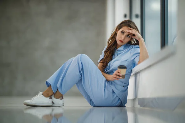 Fotografía Una Joven Enfermera Cansada Sentada Suelo Cerca Una Ventana —  Fotos de Stock