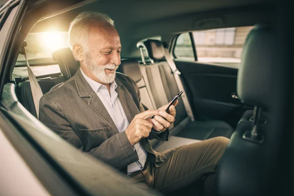 朝の通勤中に車の後部座席に座っている間にスマートフォンを使用して成功したシニアビジネスマンのショット — ストック写真