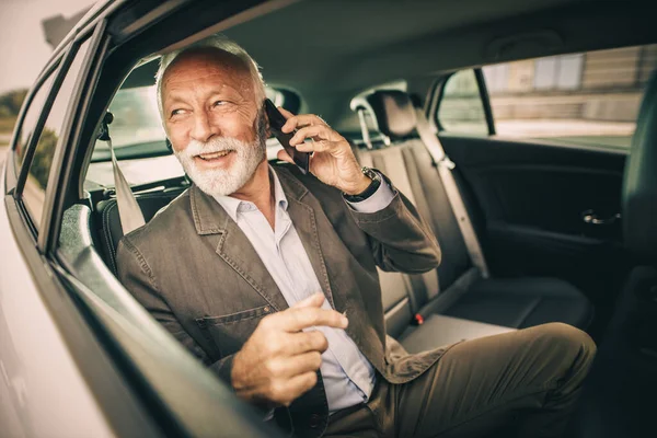 彼の朝の通勤中に車の後部座席に座っている間にスマートフォンで話して成功した先輩ビジネスマンのショット — ストック写真