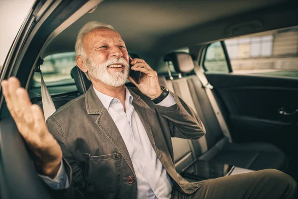 通勤中に車の後部座席に座っている間にスマートフォンで話している成功した先輩のショット — ストック写真